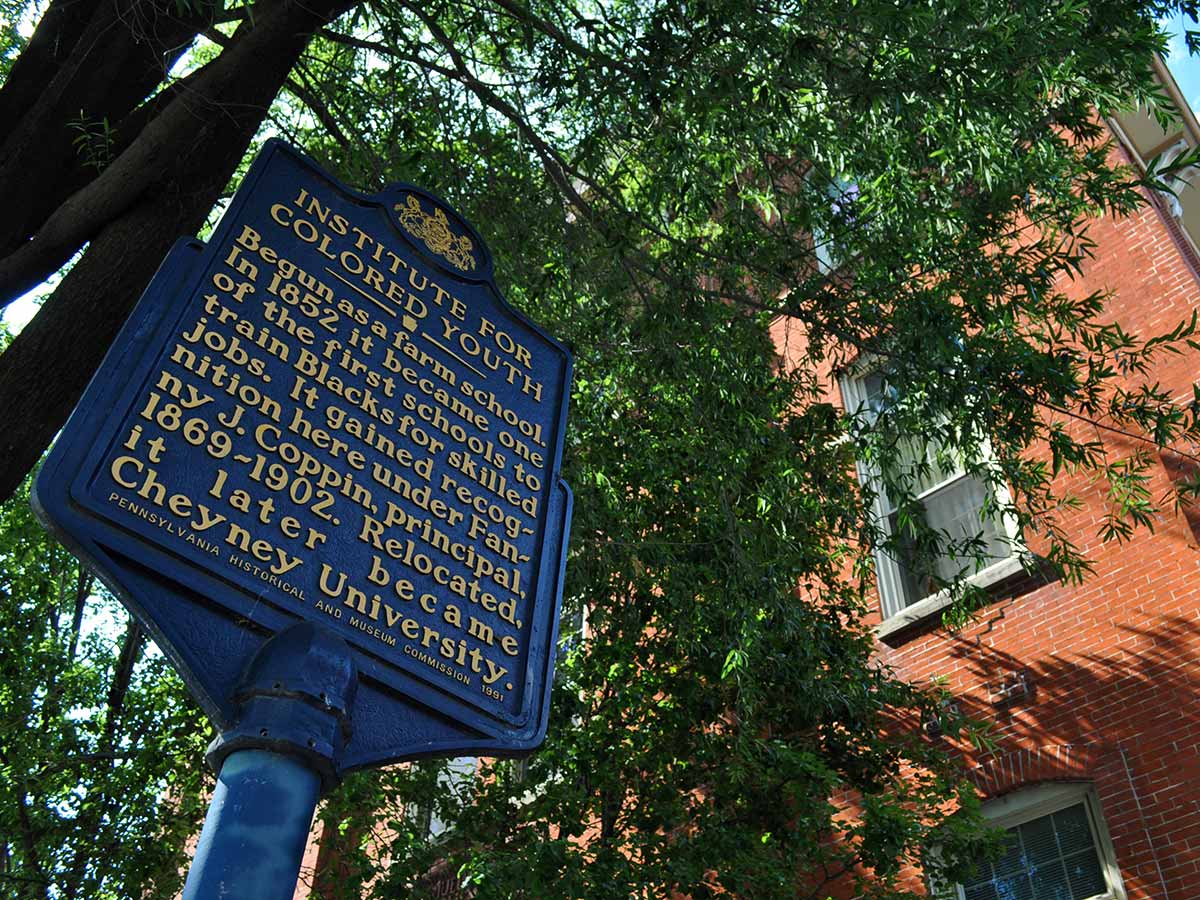 Historical marker for the Institute for Colored Youth in front of a brick building and leafy trees.
