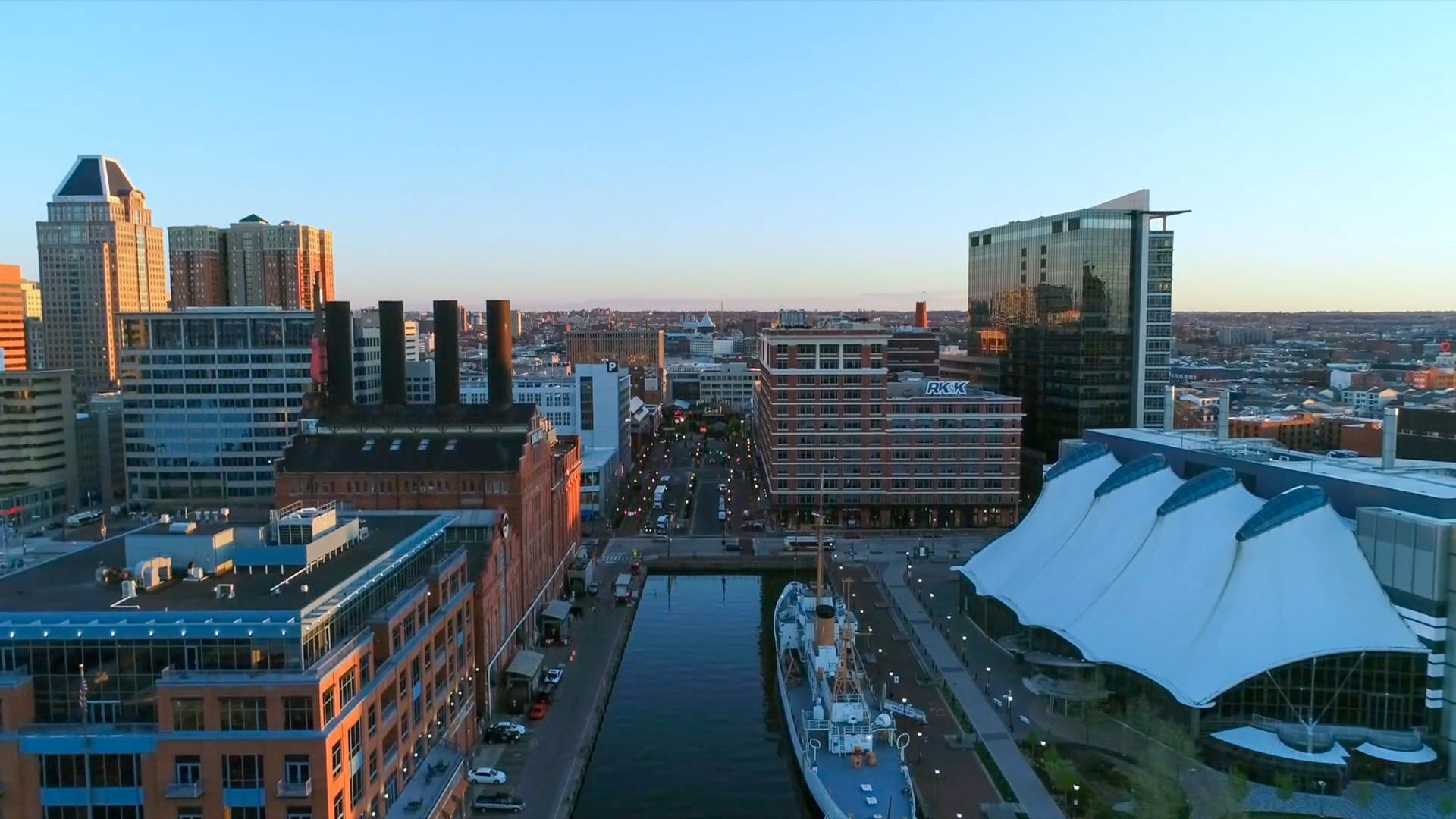 Aerial view of a waterfront cityscape with tall buildings, brick structures, and a docked ship along a narrow harbor.