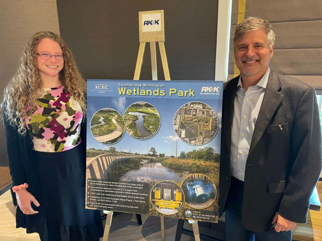 A man and a woman standing next to a poster with facts about the Southbridge Wilmington Wetlands Park.