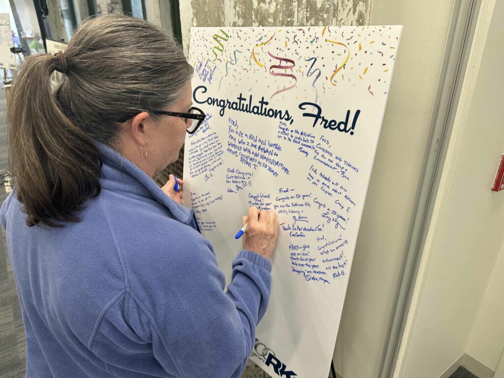 A woman signing a poster for Fred Schutte with notes congratulating him on his 50-year anniversary