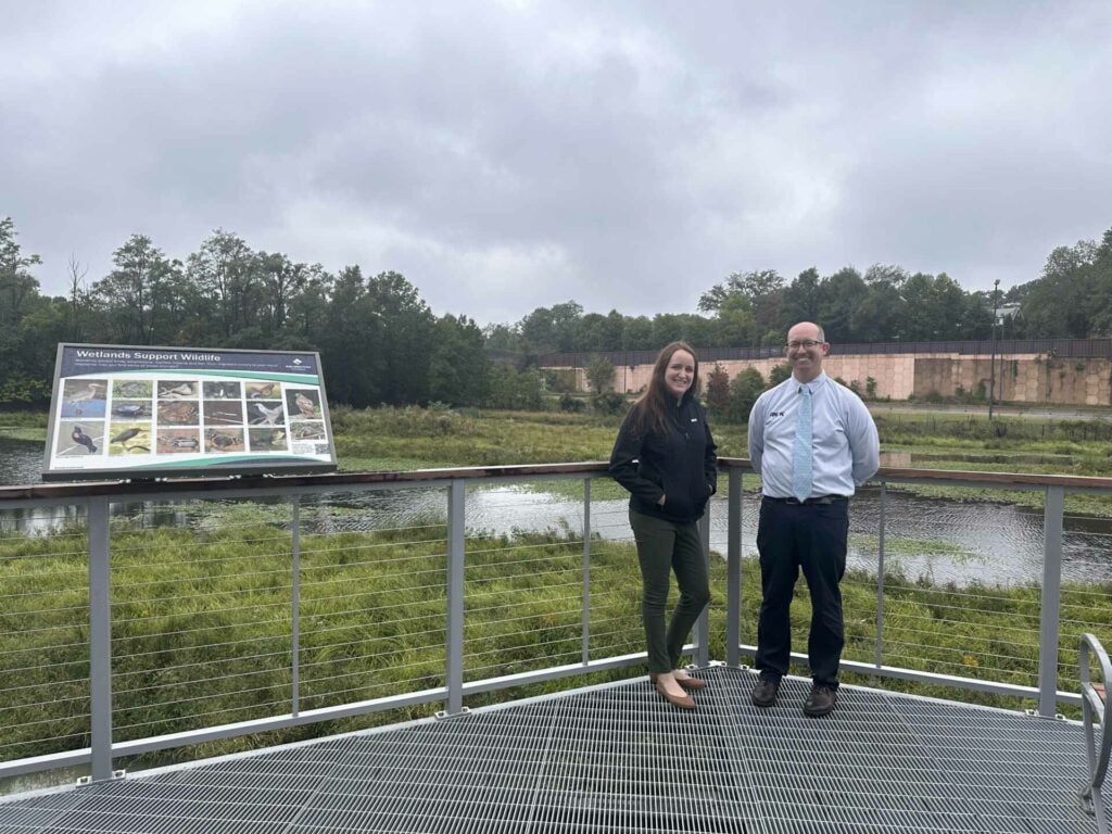 a man and woman standing next to a fence and a field