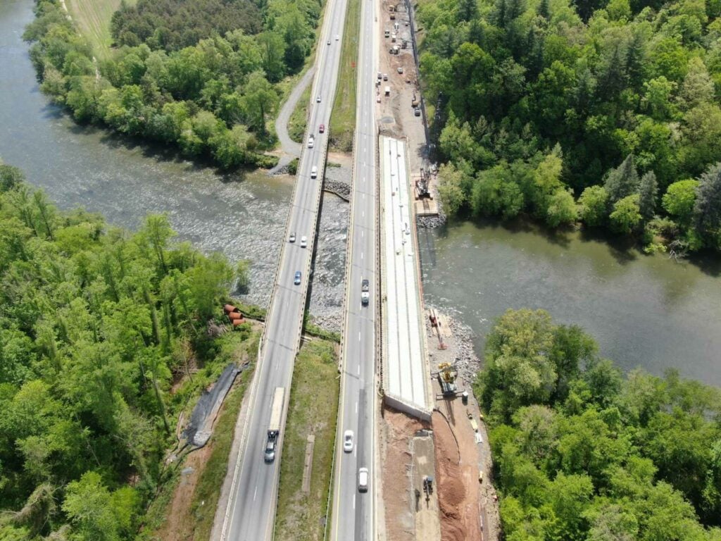 a road with cars on it next to a river with trees