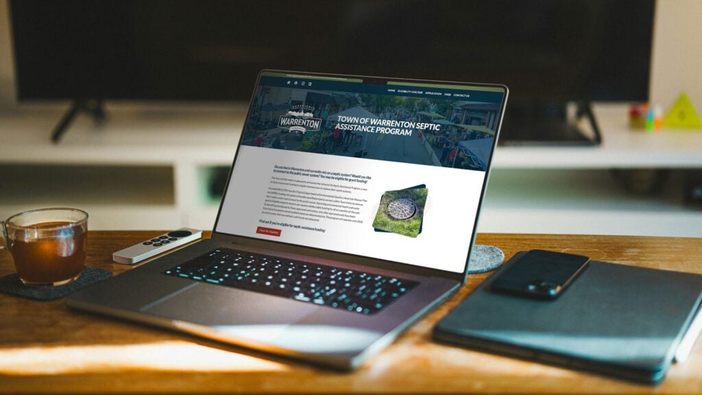 A laptop on a desk showing the Warrenton Septic Assistance Program website.