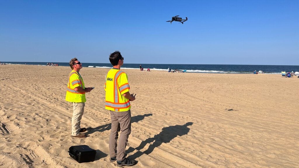 Two men on a beach watching a drone.