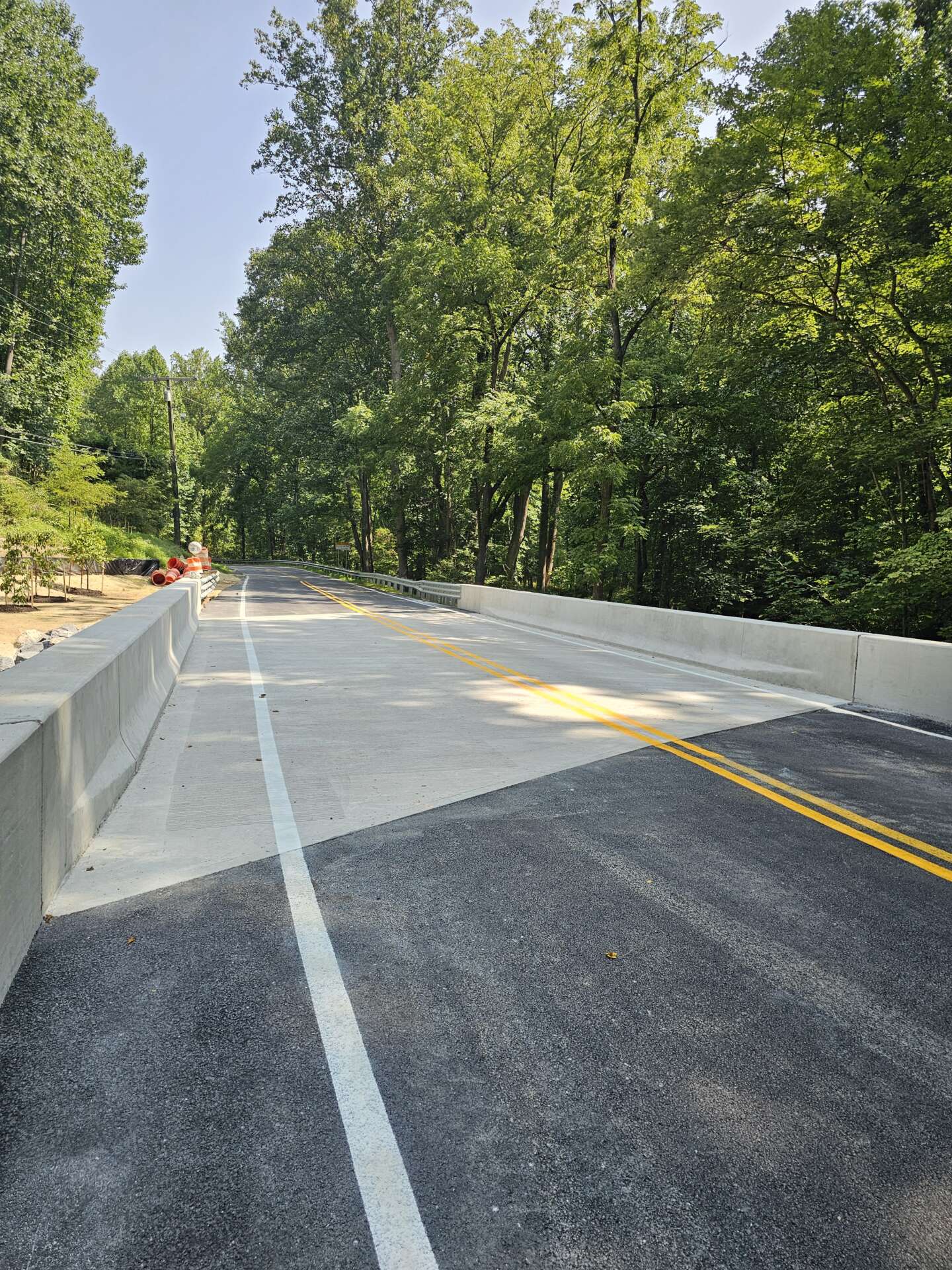 Completed Henryton Road bridge with fresh pavement, concrete barriers, and lane markings through a tree-lined corridor.