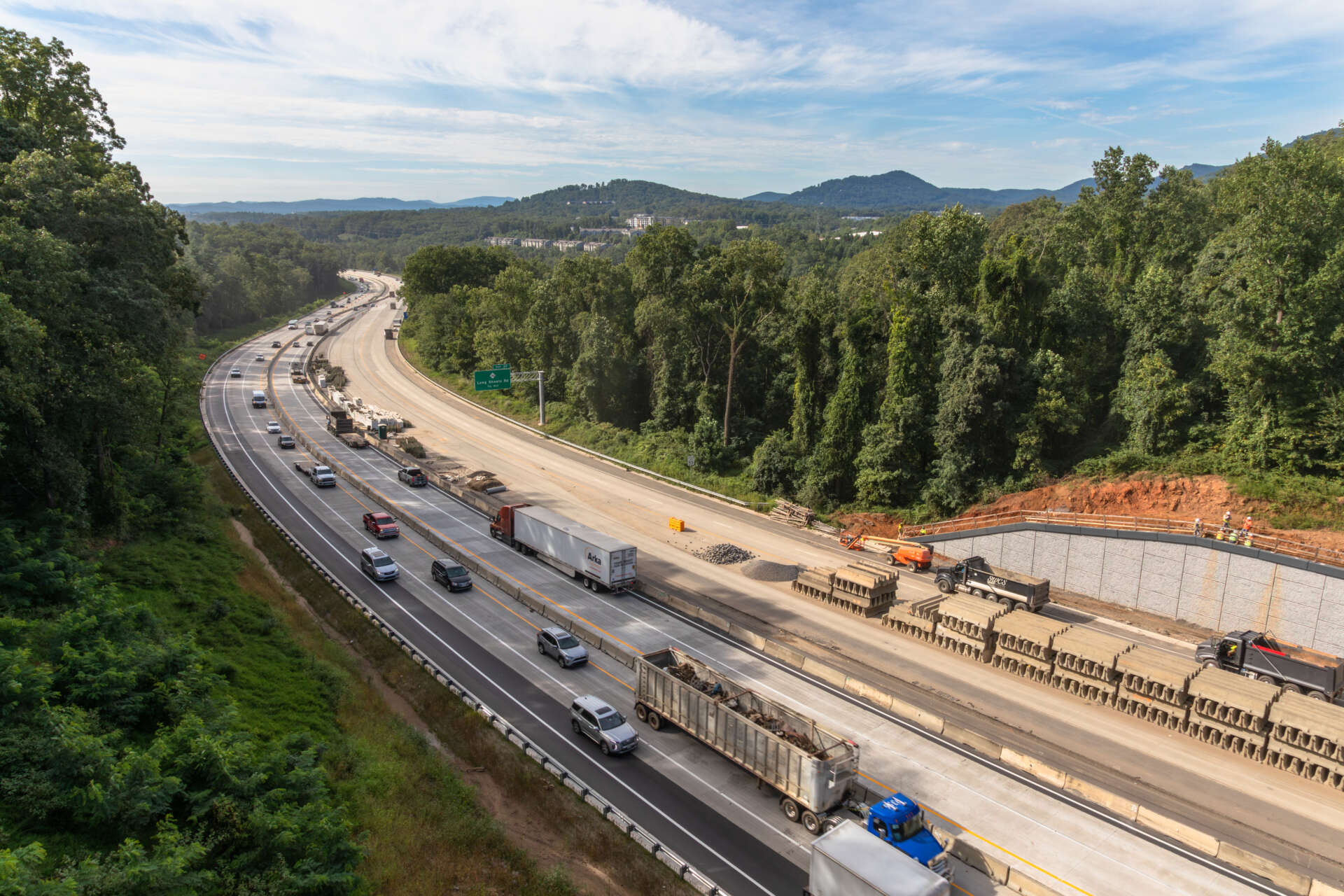 Highway construction crews expand lanes along the I‑26 Asheville Connector, highlighting North Carolina’s $1.2 billion flagship design‑build project cutting through a mountainous, forested corridor.
