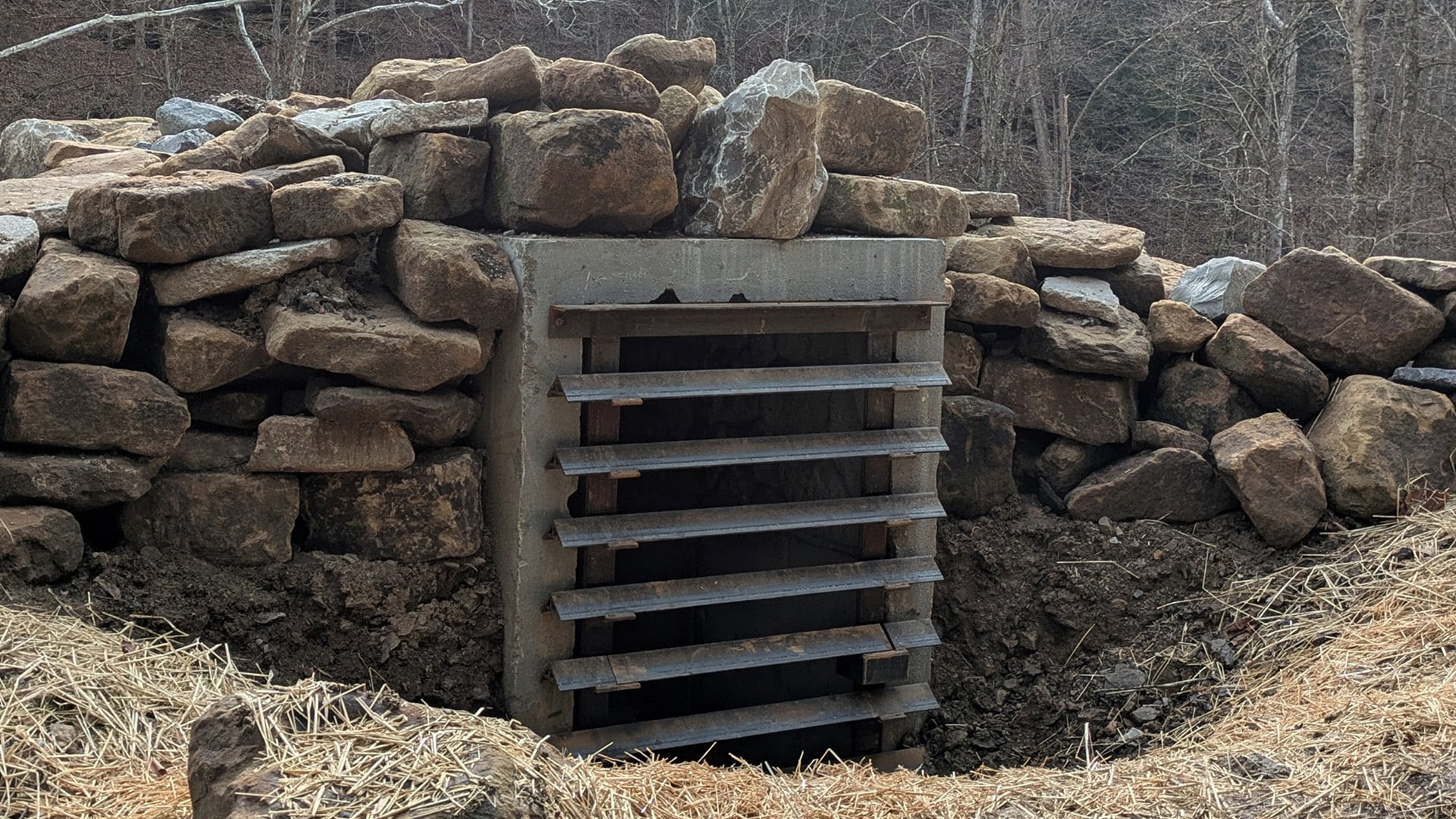 Bat hibernaculum entrance with metal grates surrounded by stacked boulders and earth.